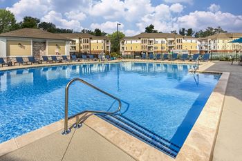 A swimming pool with a metal ladder in the foreground and apartment buildings in the background